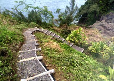 downward view of stairwell made of logs and gravel winding up a hill overlooking the ocean